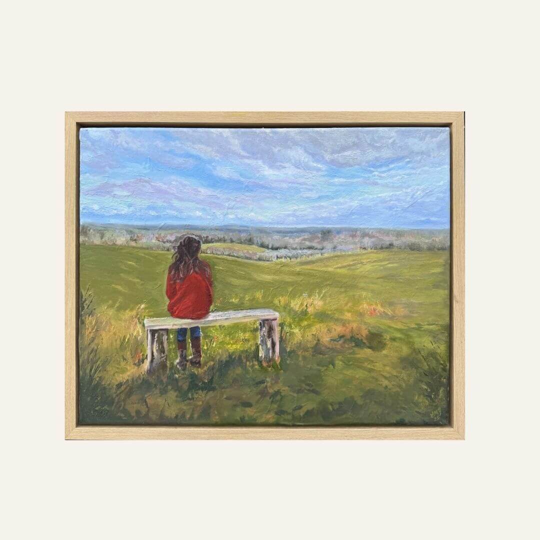 Framed oil painting "If Fields Could Talk", showing a woman seated on a bench overlooking the countryside.