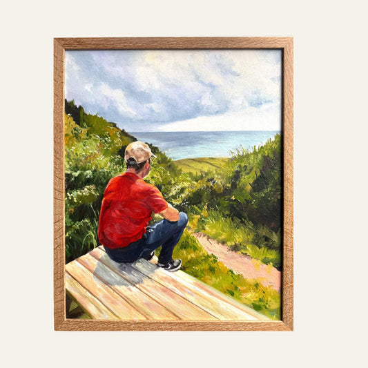 Framed original coastal painting Just Taking It In by Lorraine Field, showing a seated man in red overlooking green cliffs and a blue-grey sea.