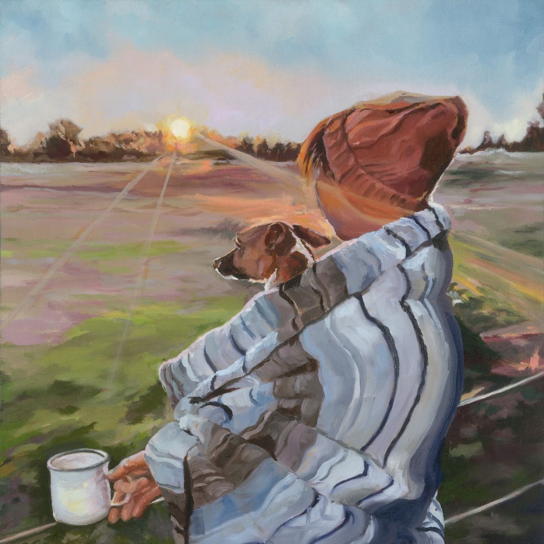 Person under a striped blanket with a dog, looking at a sunset over a field.
