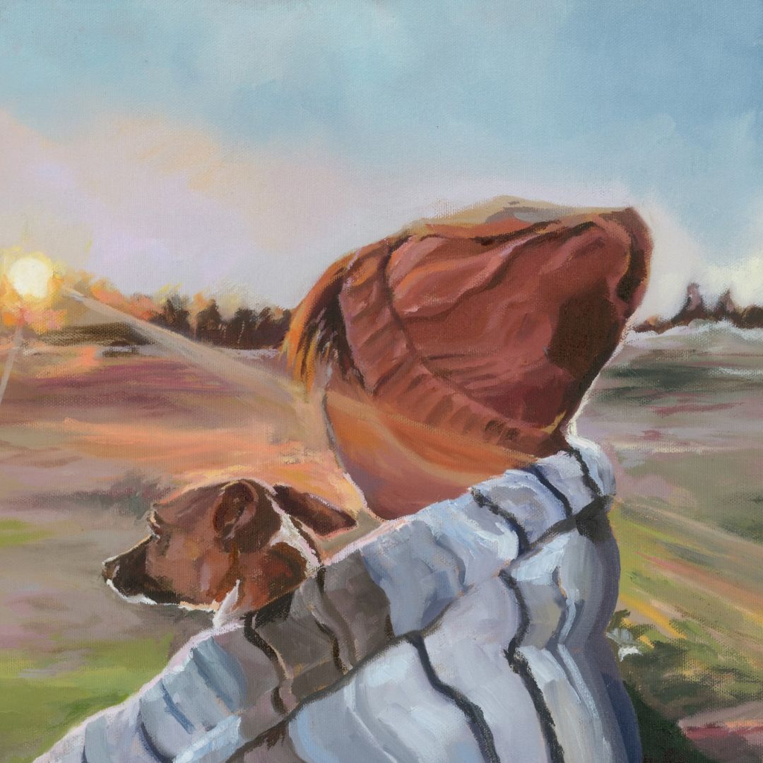 Person with a dog wrapped up in a striped blanket together watching the sunrise