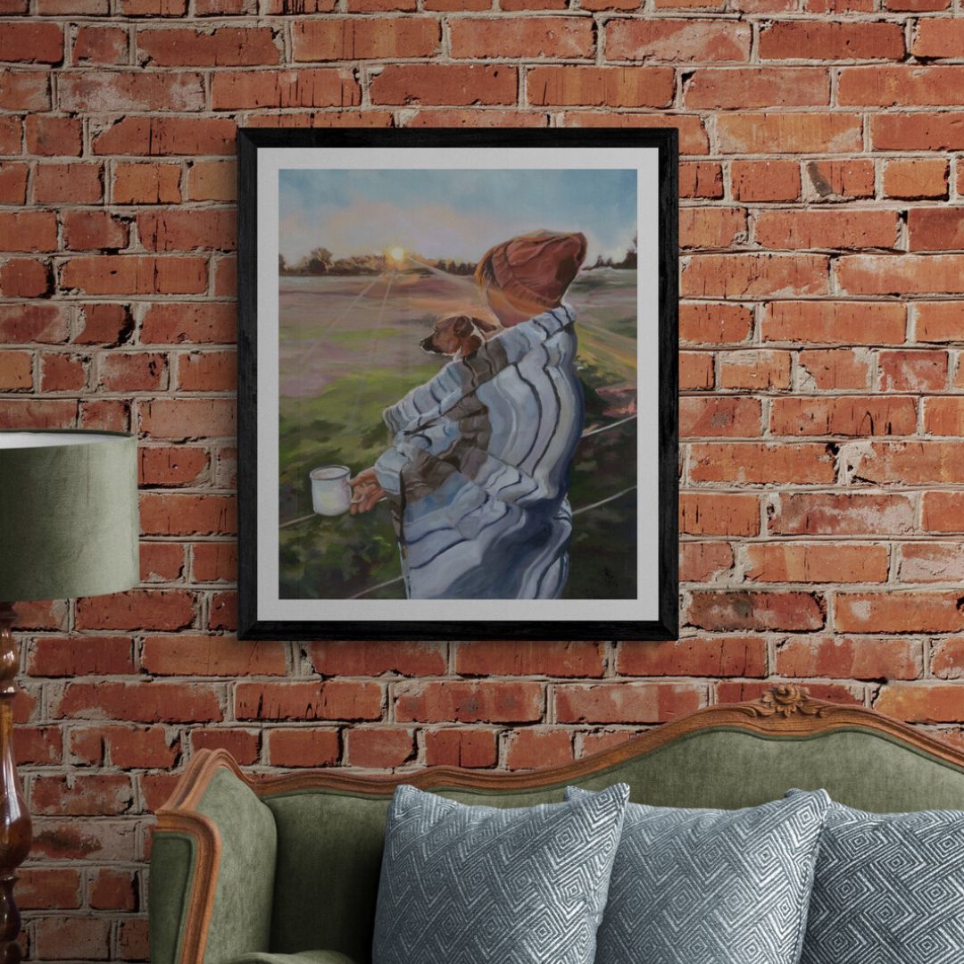 Framed artwork of a person with a dog watching sunrise together, displayed on a brick wall above a sofa.