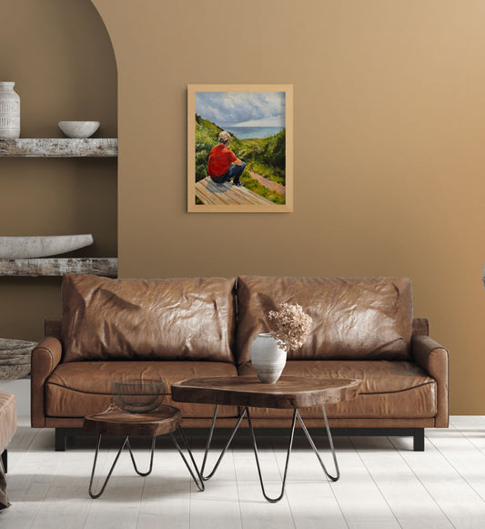 Framed Just Taking It In coastal oil painting by Lorraine Field, displayed above a brown leather sofa in a warm, earthy living room.
