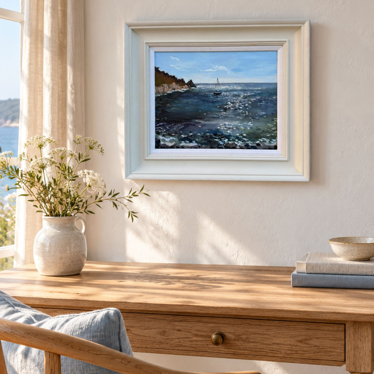 Room mockup showing Lorraine Field’s framed Lamorna Cove seascape above a sunlit oak desk in a coastal interior.