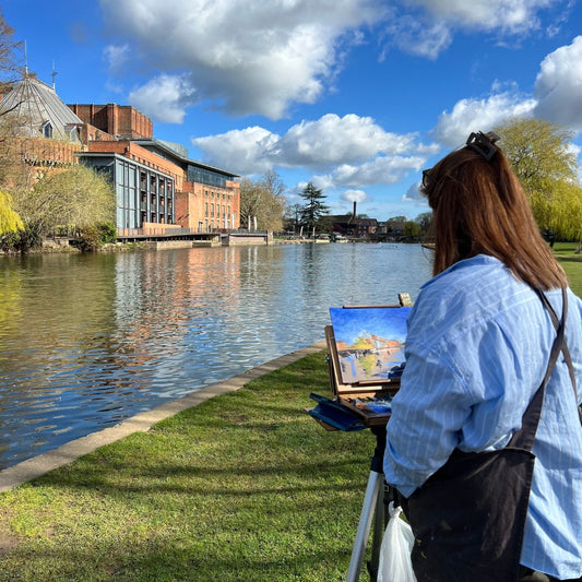 Artist Lorraine Field painting en plein air by the River Avon in Stratford-upon-Avon with the Royal Shakespeare Theatre in view