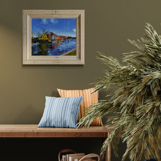 oil painting of the Royal Shakespeare Theatre in Stratford-upon-Avon displayed on a green wall above a wooden bench with cushions