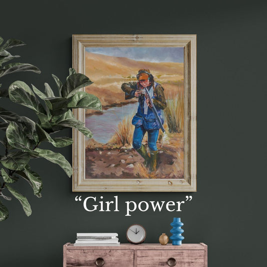 Framed artwork of a young girl shooting clays in a natural setting with 'Girl power' text below on a dark wall.