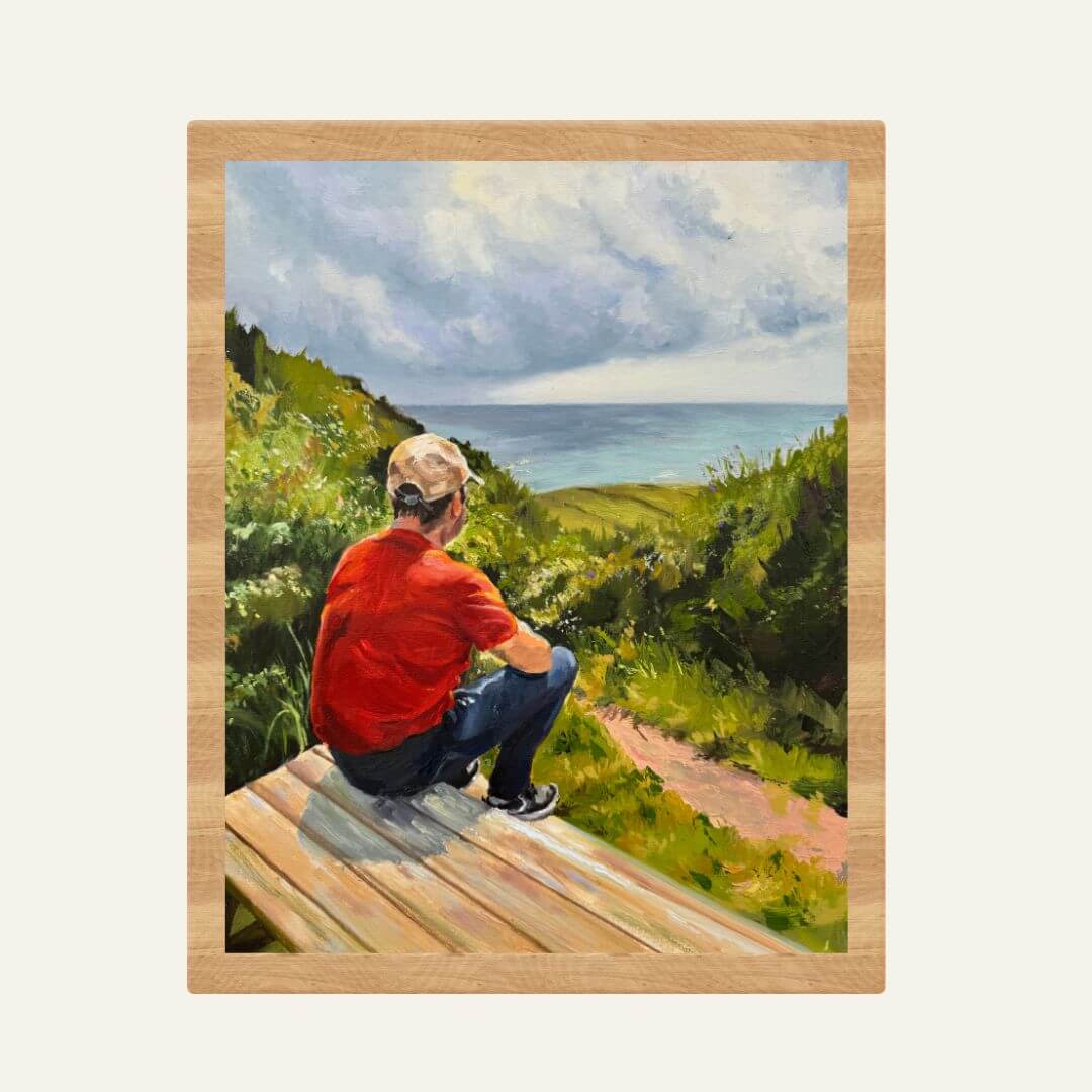 Framed original coastal painting Just Taking It In by Lorraine Field, showing a seated man in red overlooking green cliffs and a blue-grey sea.
