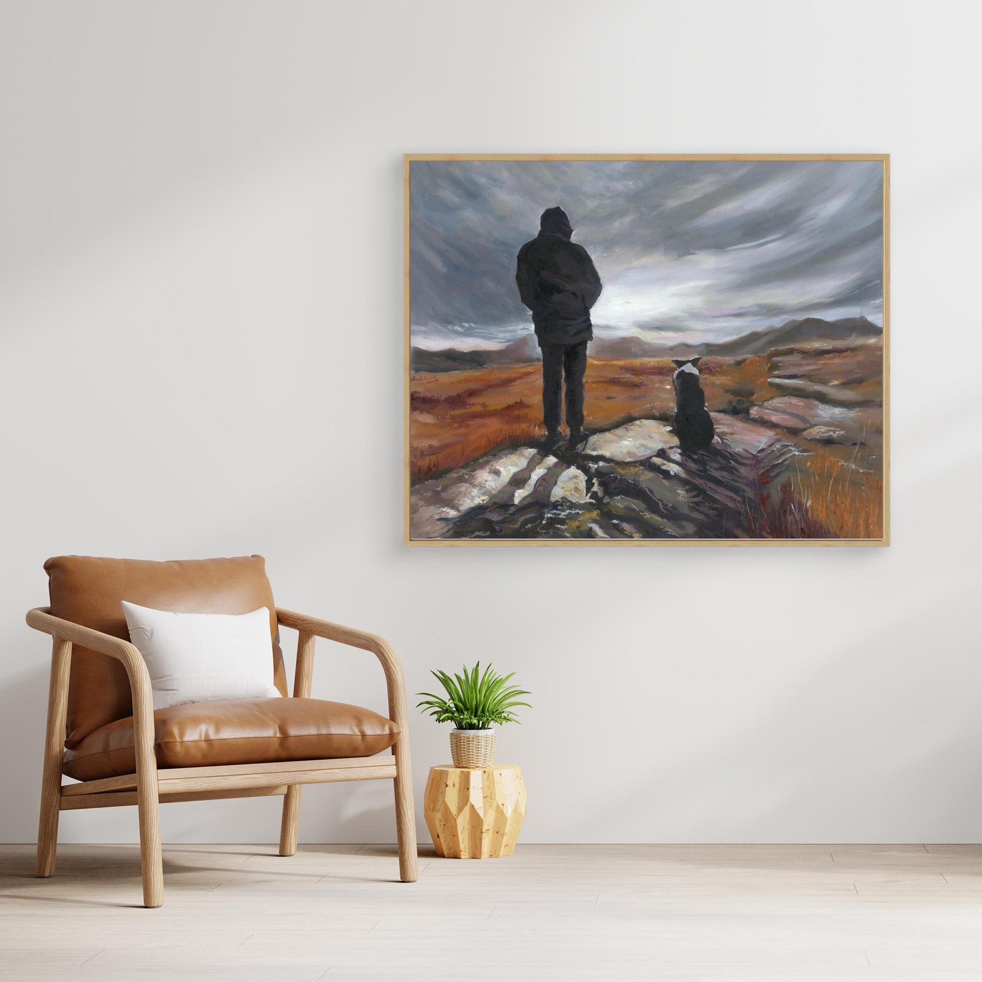 Room interior with a brown armchair, plant, and a large painting of a man and Border Collie dog on a landscape.