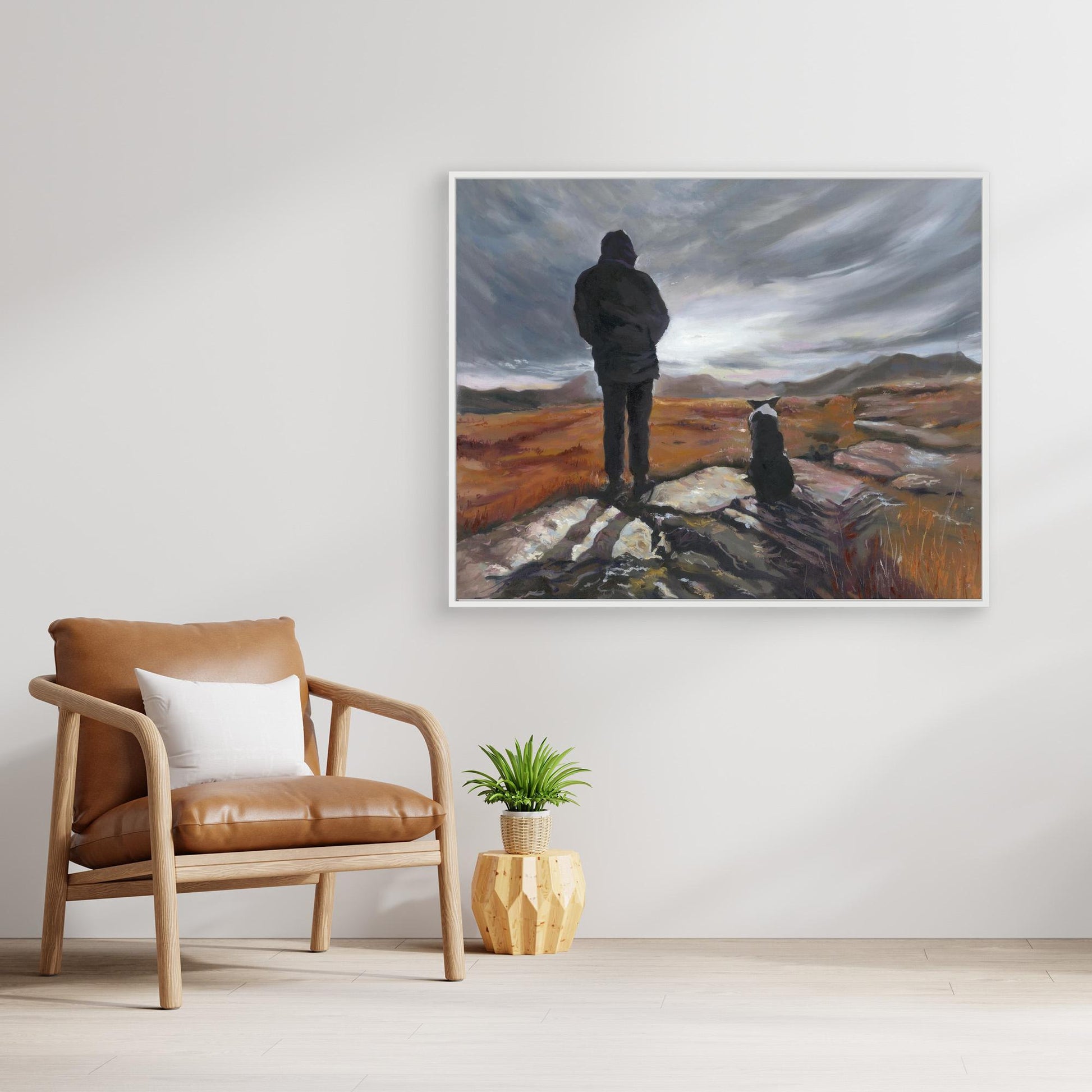 Room interior with a brown armchair, small table with plant, and framed canvas print of a man and Border collie dog on a landscape.