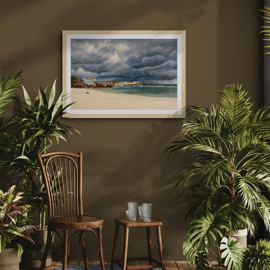 Framed art print of a Porthminster Beach  stormy cloud scene on a wall with plants and a wooden chair in the foreground.