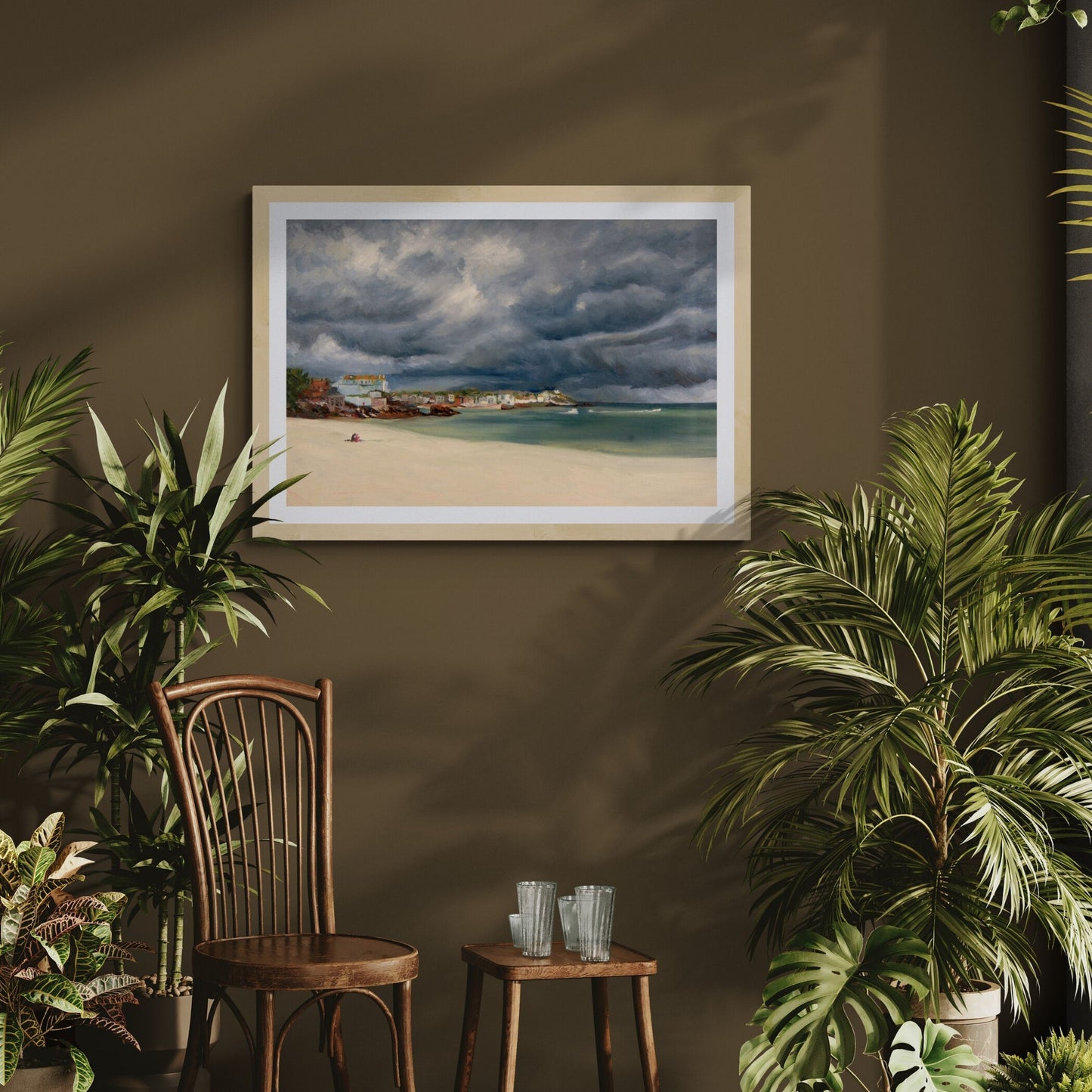 Framed art print of a Porthminster Beach  stormy cloud scene on a wall with plants and a wooden chair in the foreground.