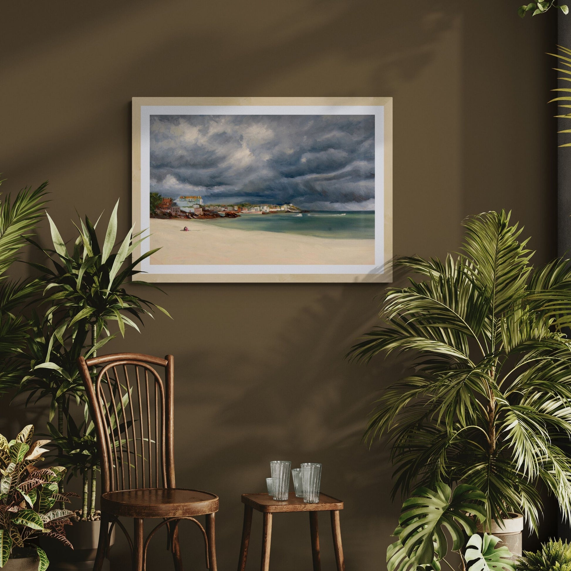 Framed art print of a Porthminster Beach  stormy cloud scene on a wall with plants and a wooden chair in the foreground.