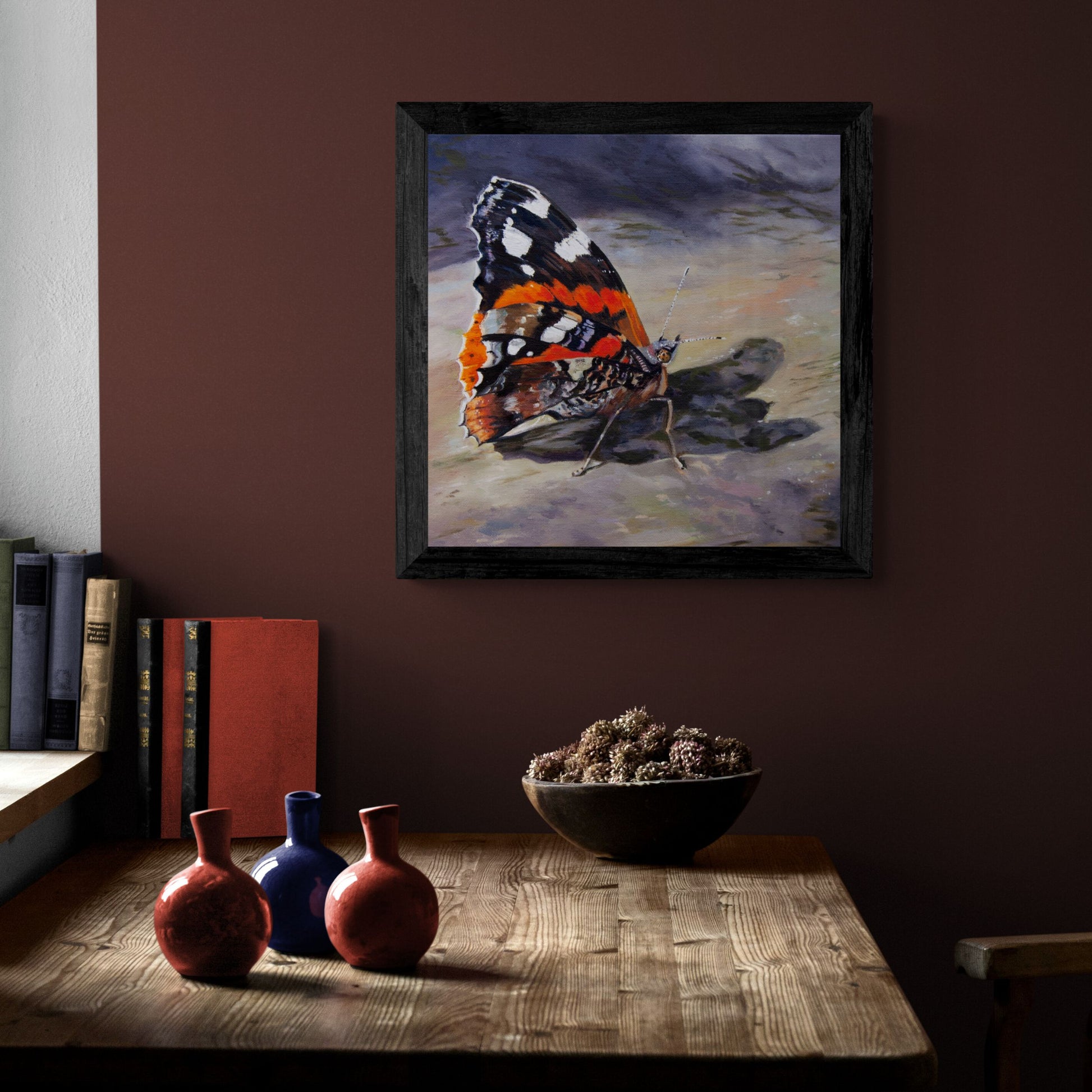 Red admiral butterfly art in black frame on dark cerise wall above wooden desk