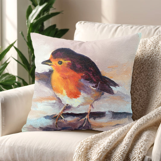 Soft pastel robin cushion on cream armchair with cosy throw. Sentimental winter home decor inspired by nature and remembrance.