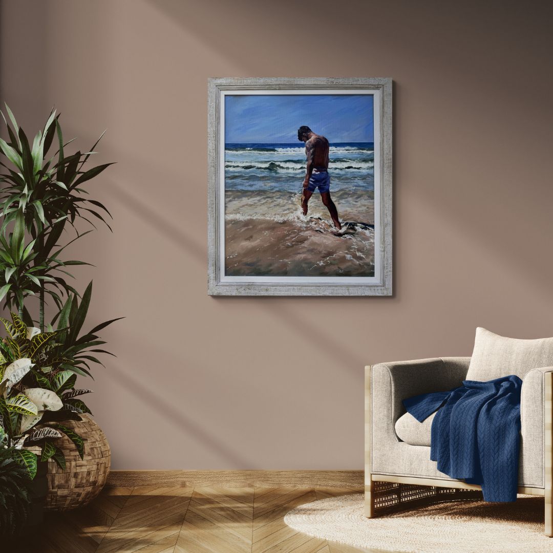 Framed original oil painting of a surfer dude man on a beach in a living room with a plant and chair.