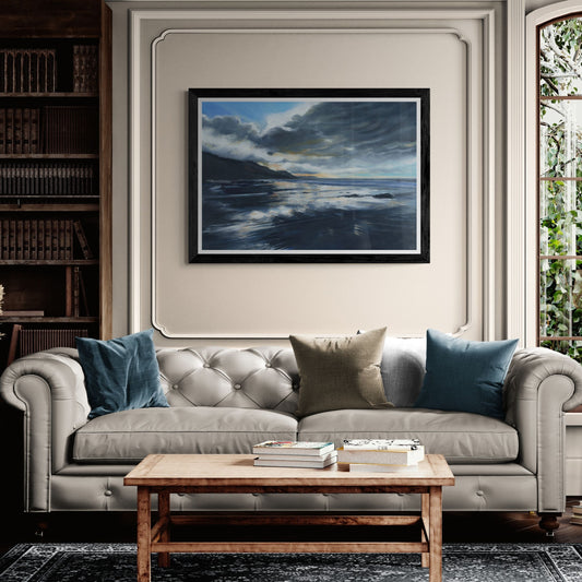Cream sofa with blue and beige pillows in a living room setting with a framed artwork of stormy seas on the wall.