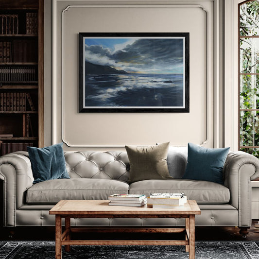 Cream sofa with blue and beige pillows in a living room setting with a framed artwork of stormy seas on the wall.