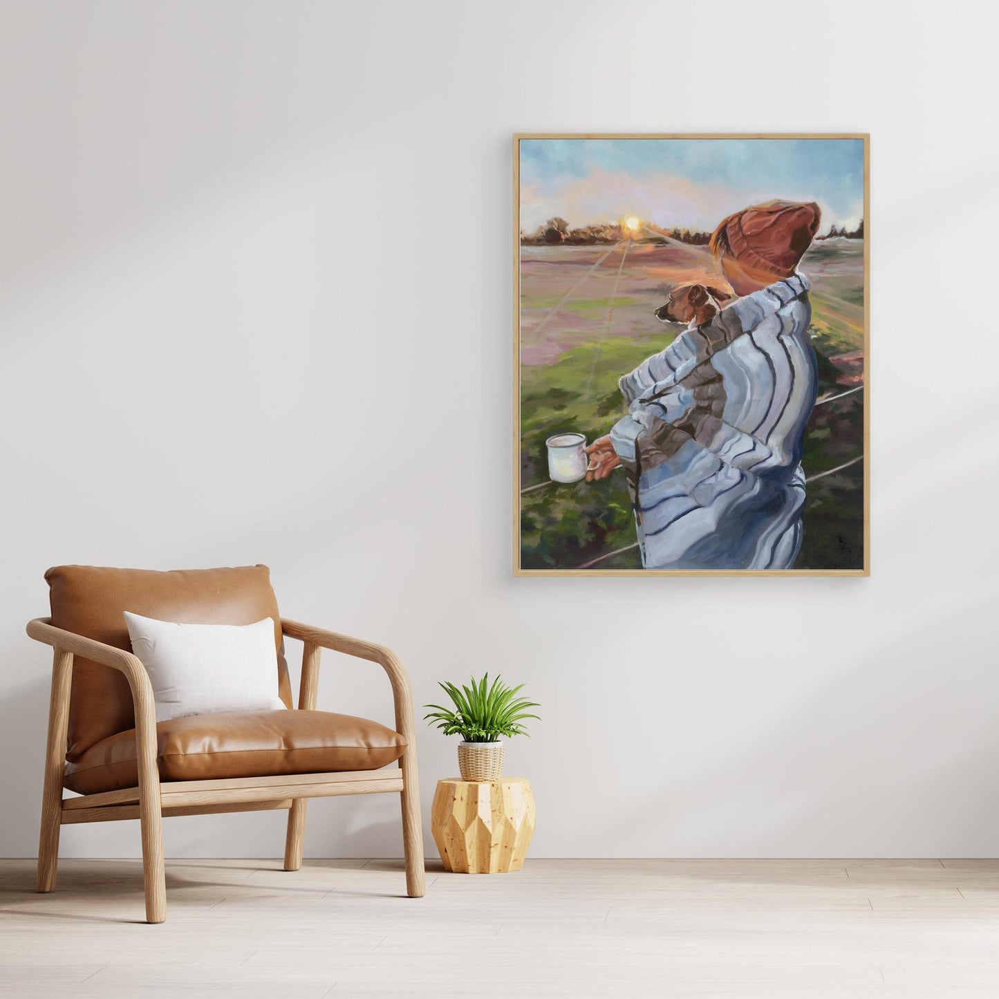 Framed artwork of a person with a Jack Russell dog on a wall in a room with a brown chair and plant.