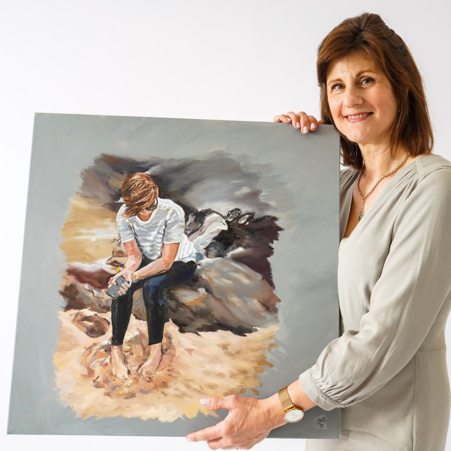 Lorraine Field Artist holding an oil painting of a young lady sitting on a rock.