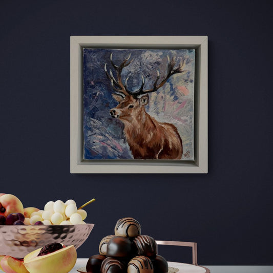 Framed painting of a deer on a dark wall with a fruit bowl and chocolate tower in the foreground.