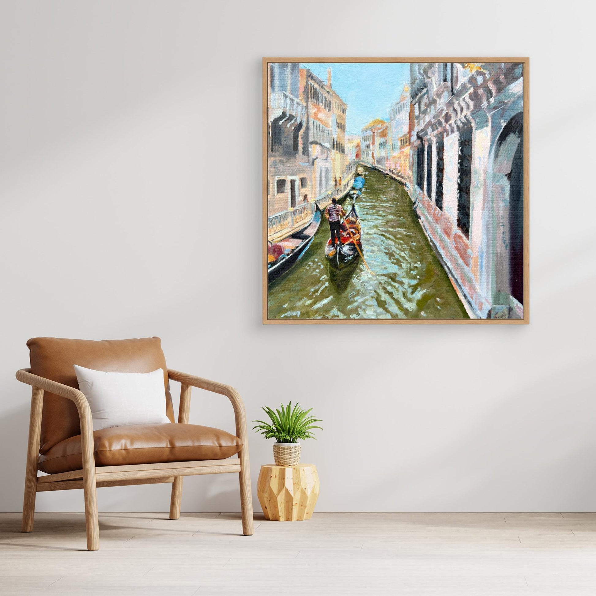 Framed painting of a Venetian canal with gondolas in a room with a brown chair and plant.