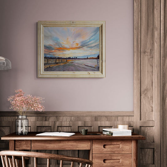 Framed fine art painting of a Warwickshire sunrise displayed above a rustic wooden desk. Cozy home office with soft neutral tones, vintage-inspired decor, and countryside landscape wall art. Perfect for nature lovers and nostalgic interior design.