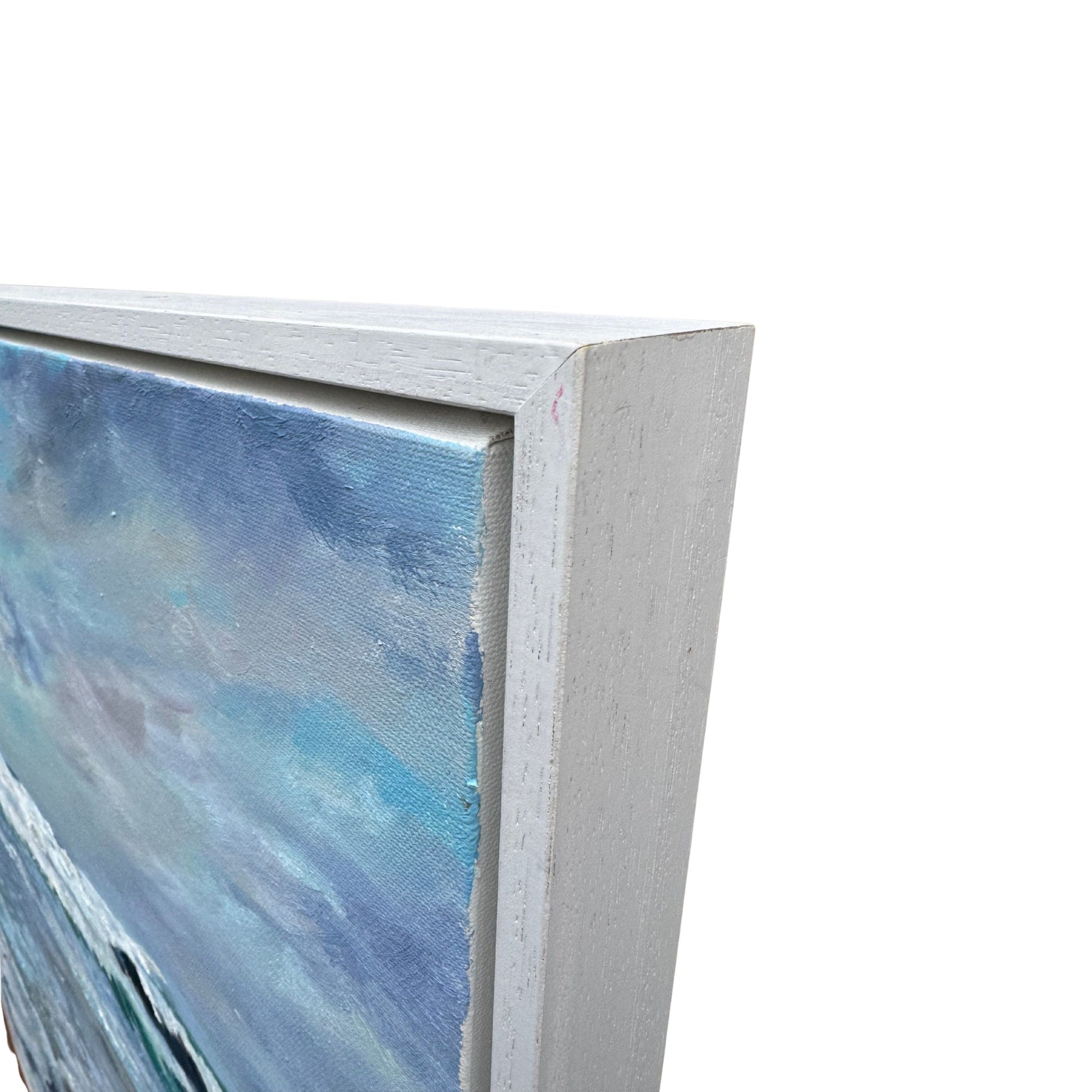 Detailed corner view of framed coastal oil painting showing canvas texture and white frame finish.