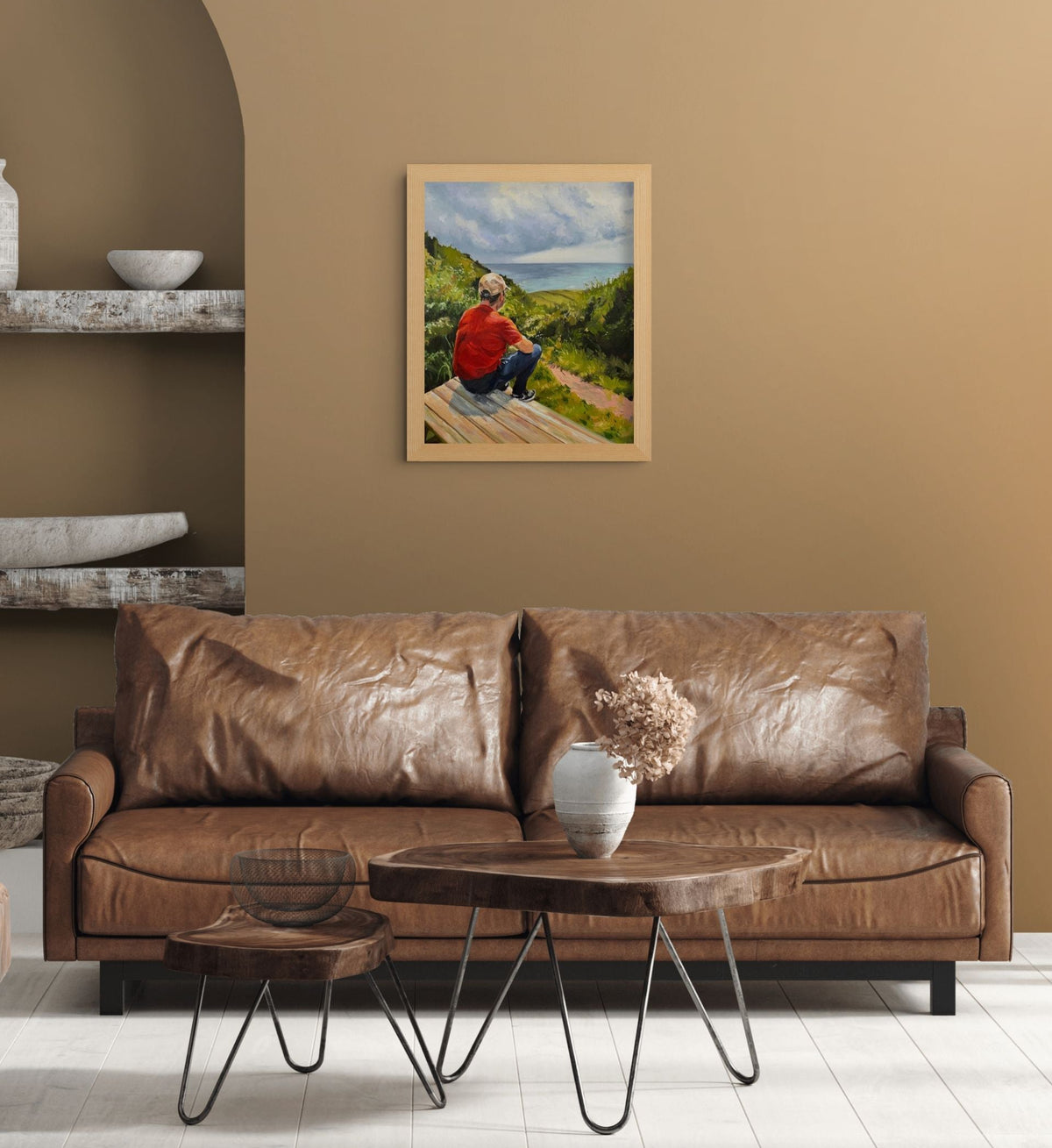 Framed Just Taking It In coastal oil painting by Lorraine Field, displayed above a brown leather sofa in a warm, earthy living room.