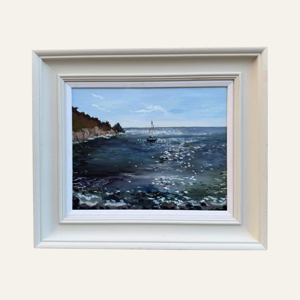 Lamorna Cove oil painting by Lorraine Field, showing a sailing boat on sparkling blue water in a pale wooden frame.