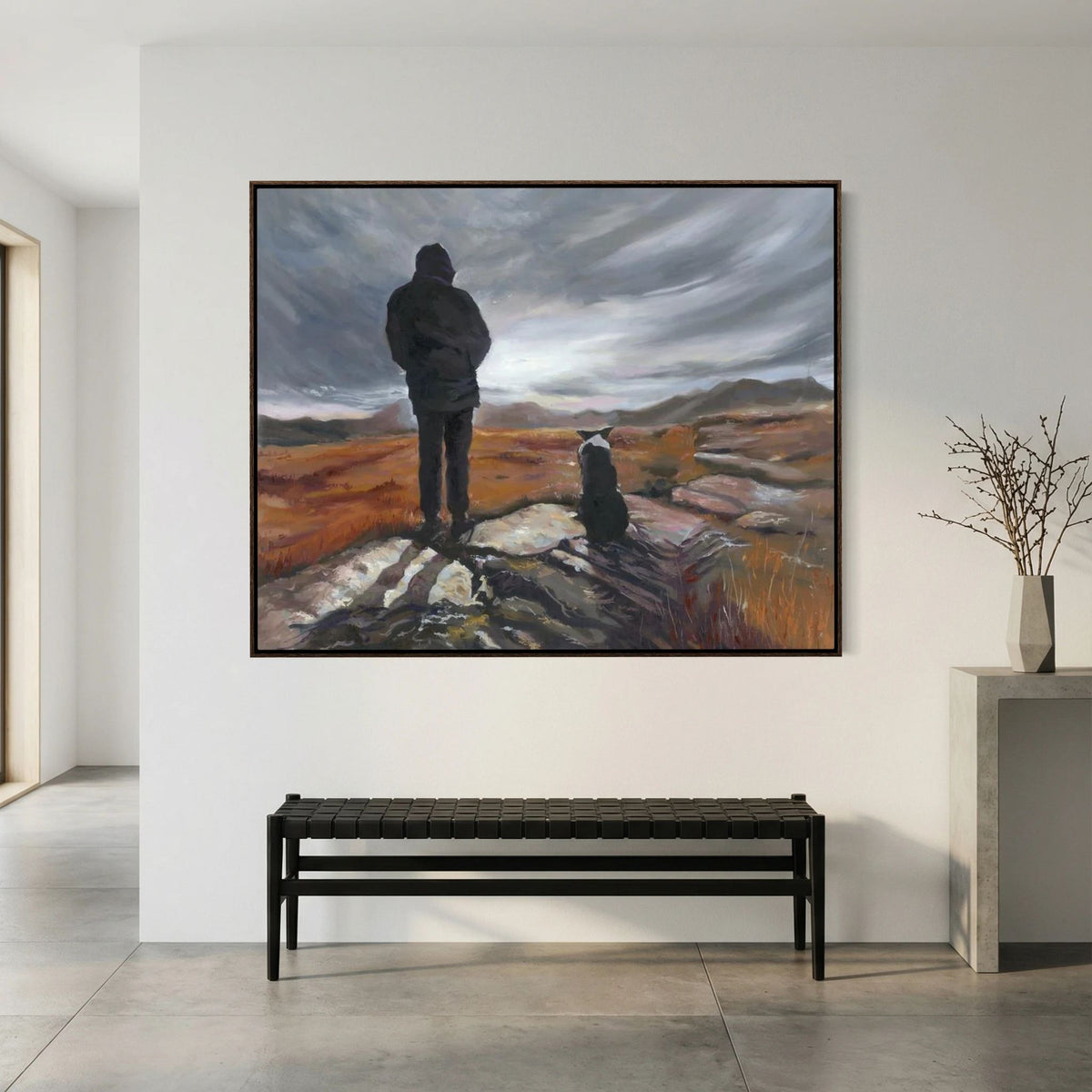 Man and His Border framed canvas print displayed above a black bench beside a tall vase of branches.