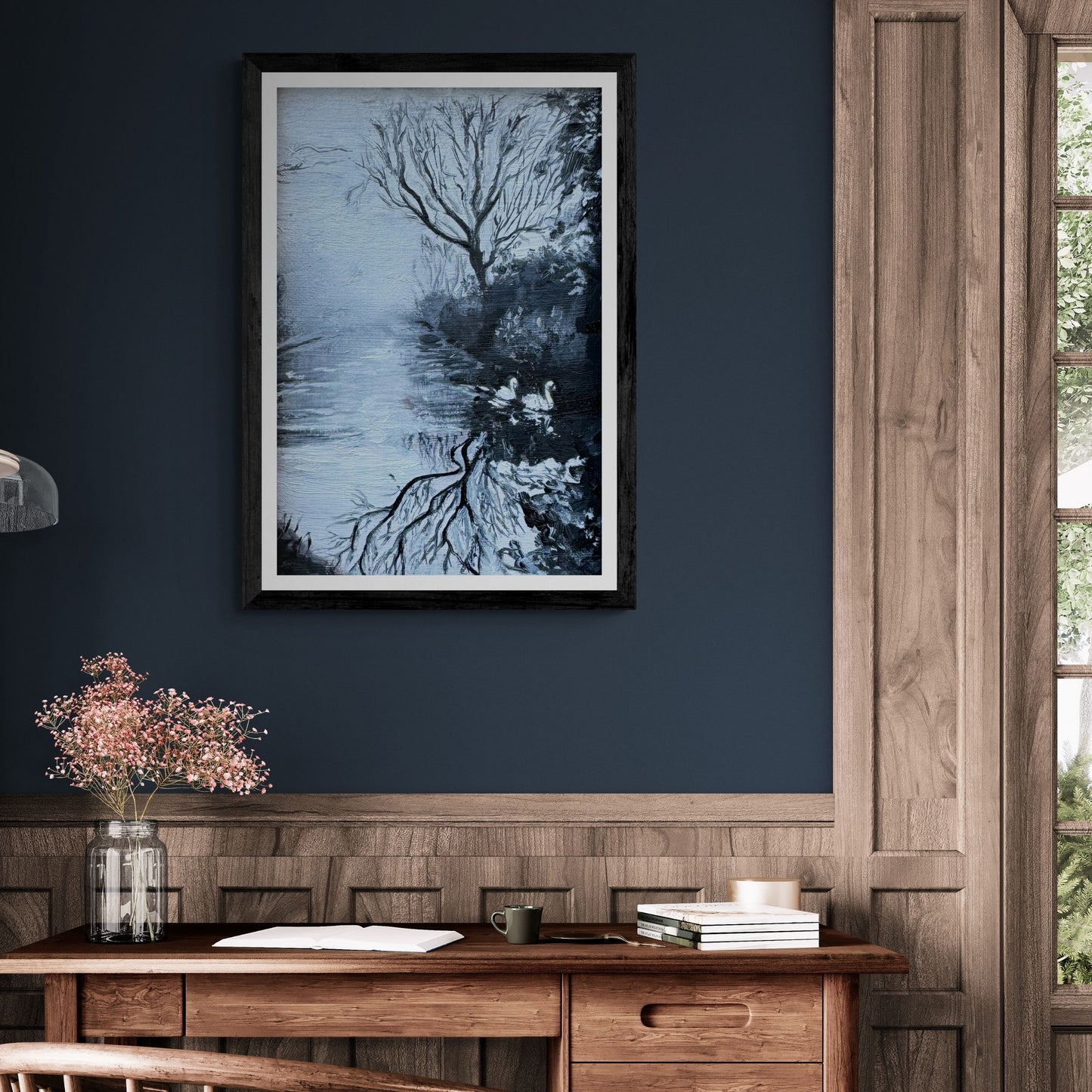 “Serenity’s Glide” swan fine art print in a black frame, styled on a deep navy wall above a wooden desk. Cool blue reflections and winter tones create a peaceful, contemplative atmosphere.
