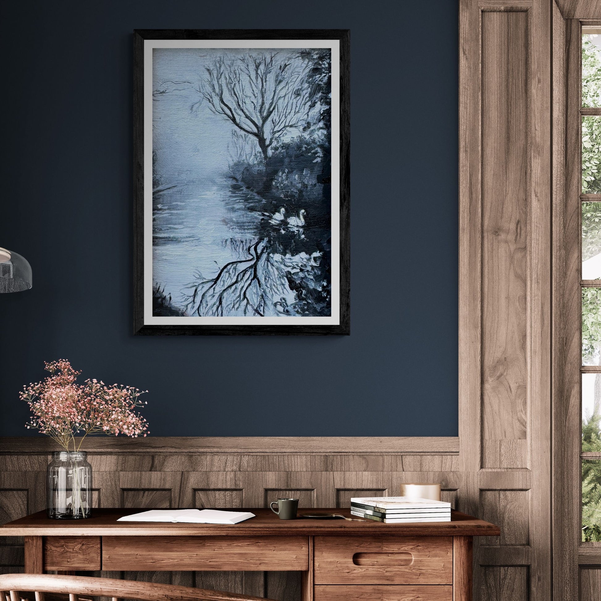 “Serenity’s Glide” swan fine art print in a black frame, styled on a deep navy wall above a wooden desk. Cool blue reflections and winter tones create a peaceful, contemplative atmosphere.